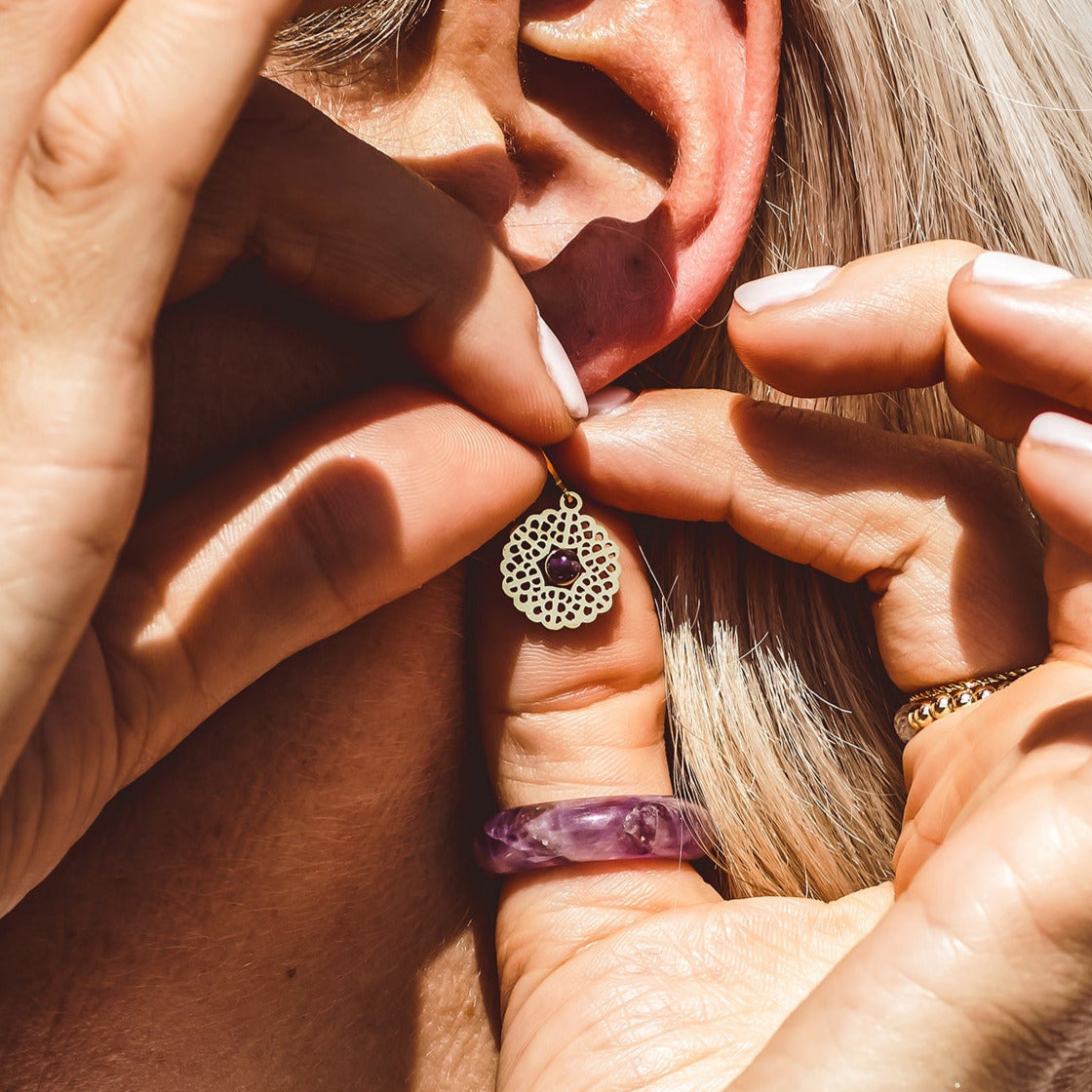 Close-up of a person holding a small gold earring near their ear.